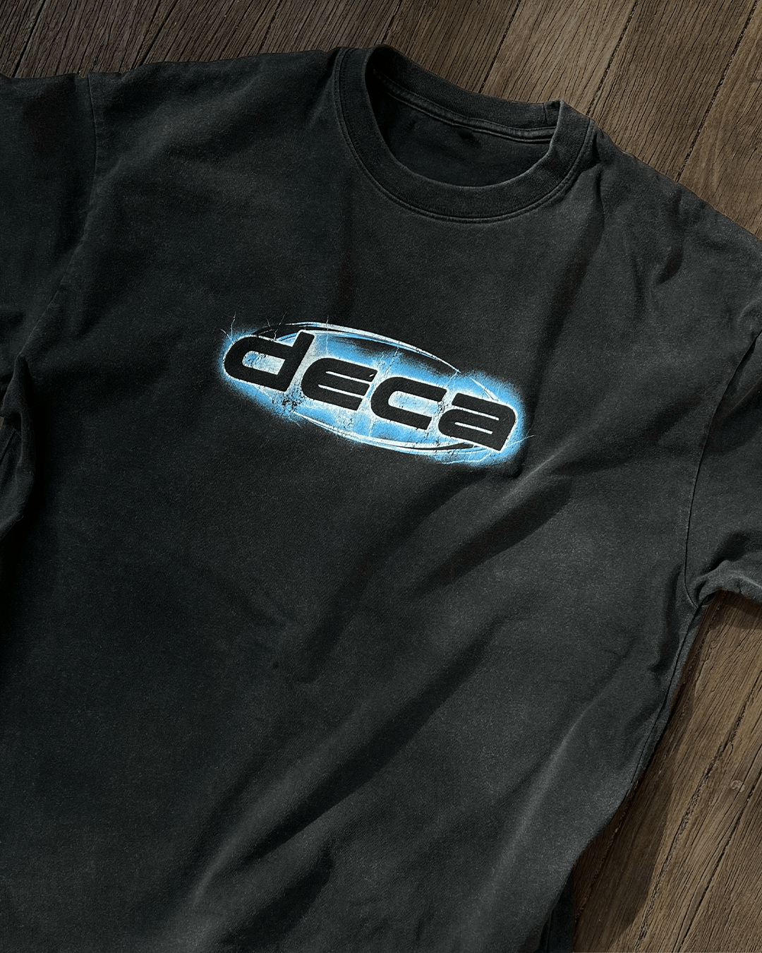 Washed black vintage tee with blue chrome DECA logo print, flat lay