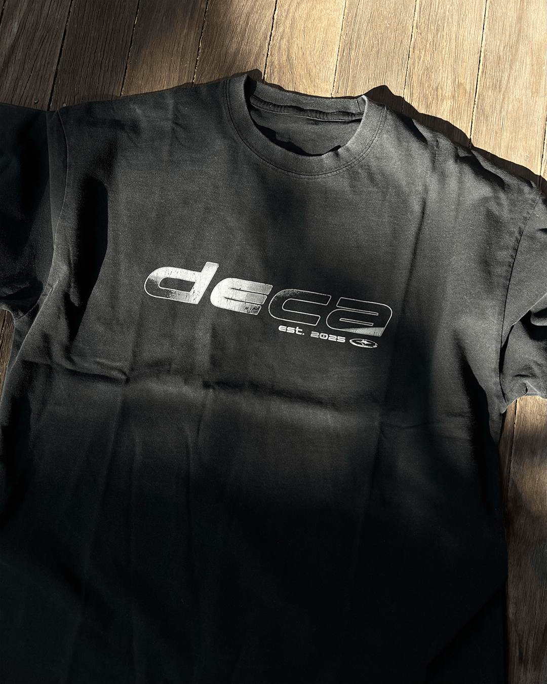 Washed black vintage tee with chrome DECA logo print, flat lay