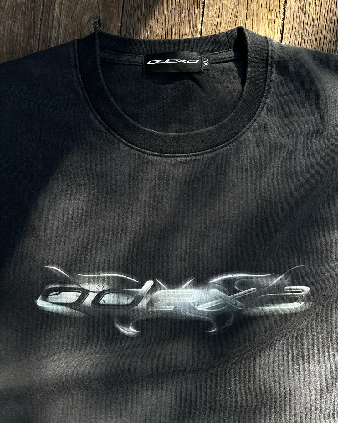 Close-up of chrome tribal ODEXA logo on washed black vintage tee