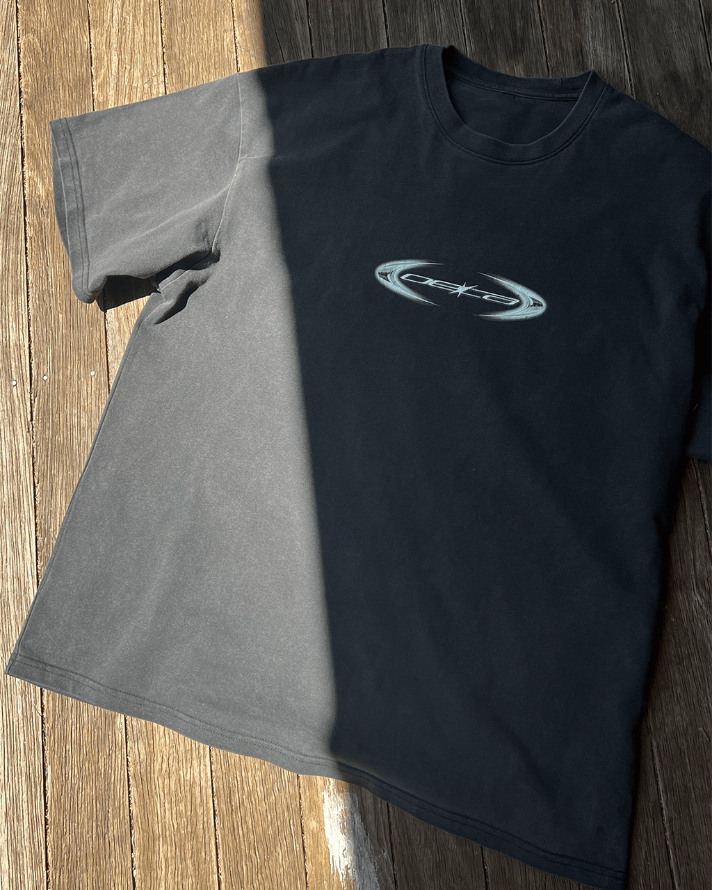 Washed black vintage tee with copper oval logo print, sunlit flat lay