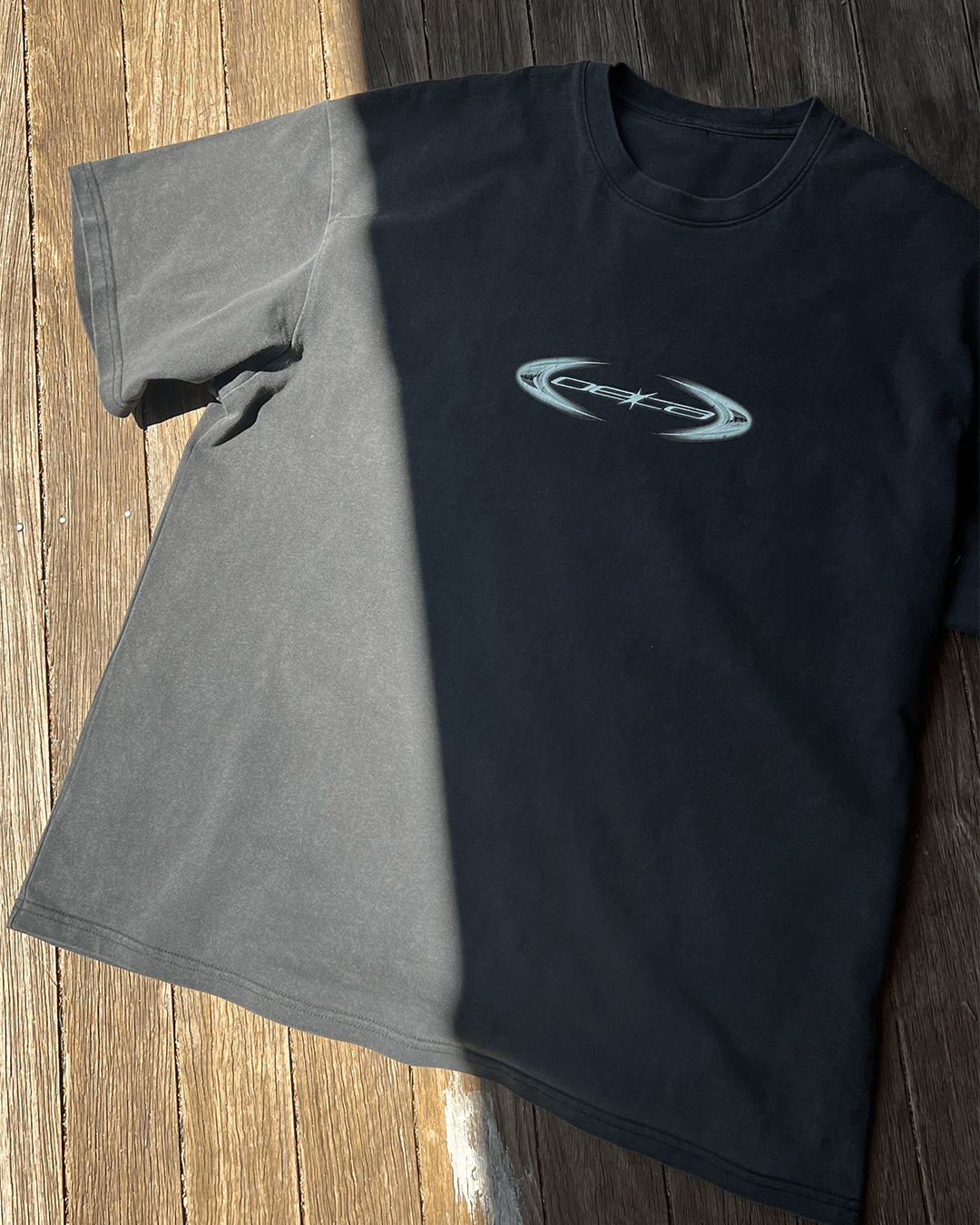 Washed black vintage tee with copper oval logo print, sunlit flat lay