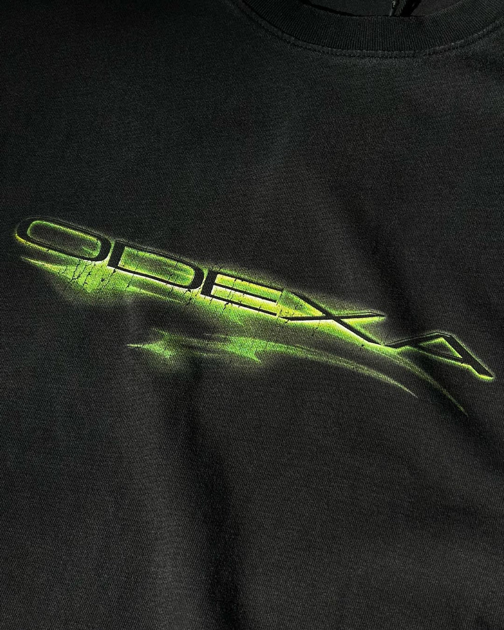 Close-up of neon green ODEXA logo print on black tee