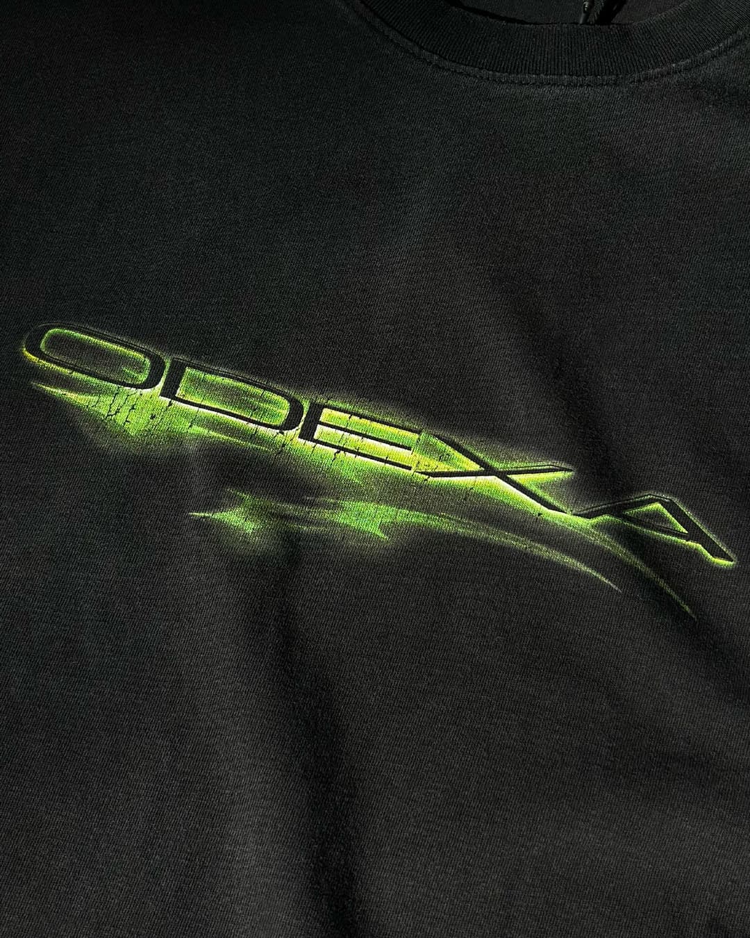 Close-up of neon green ODEXA logo print on black tee