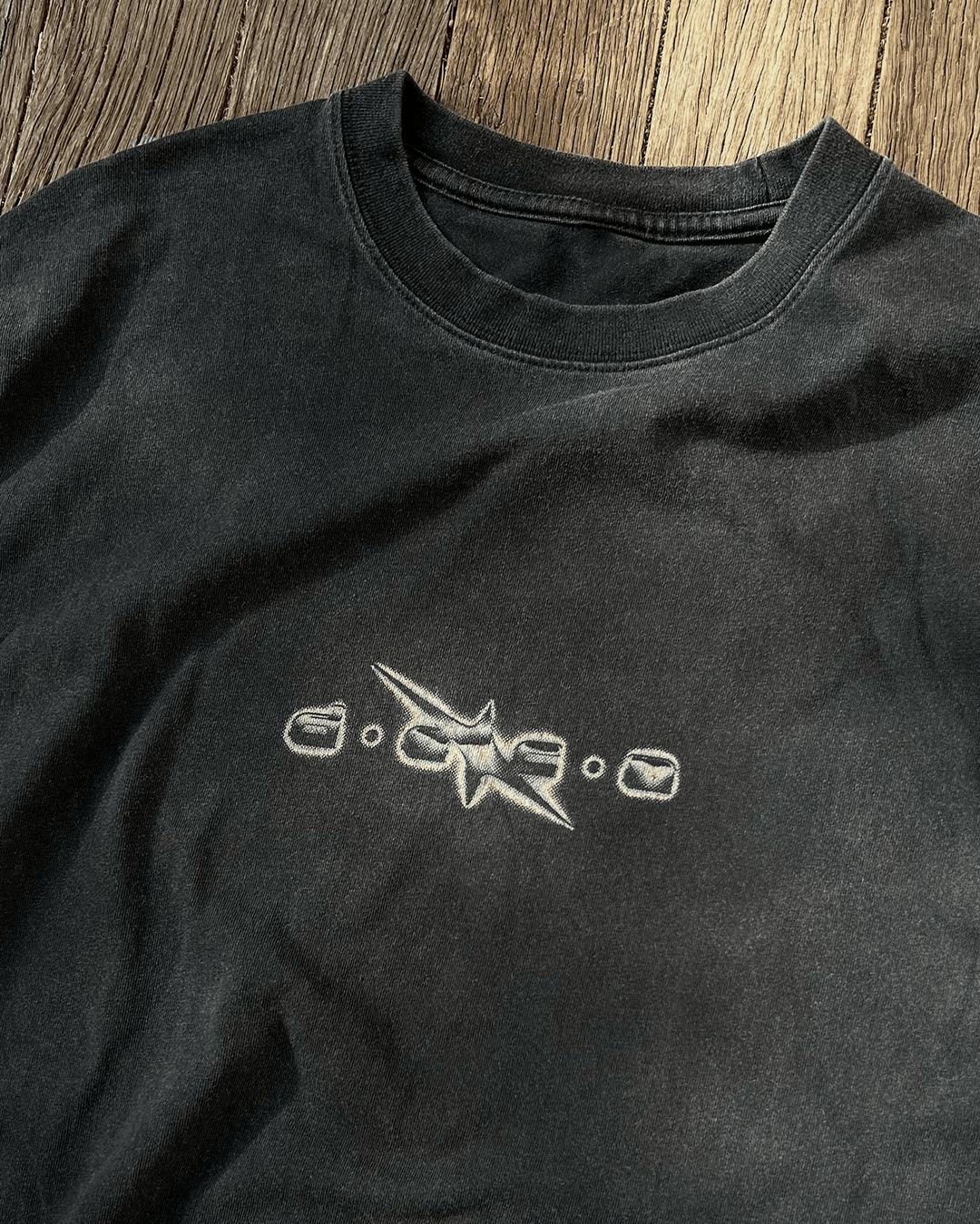 Washed black vintage tee with small grunge DECA chest logo, flat lay