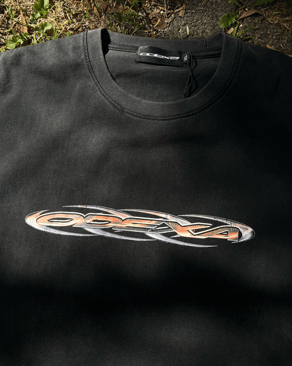 Washed black vintage tee with orange chrome tribal logo, flat lay