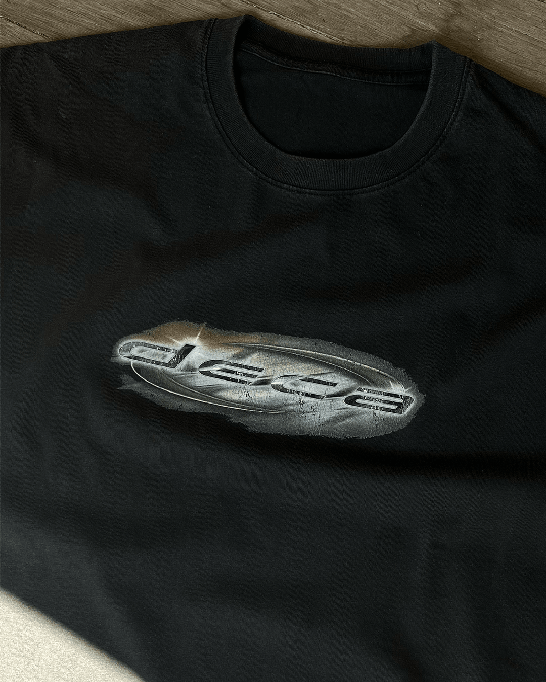 Close-up of chrome oval logo print on black Metallic Logo vintage tee